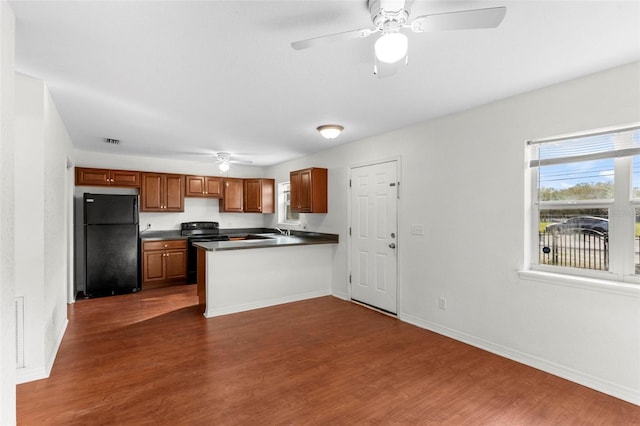 kitchen featuring dark wood finished floors, dark countertops, black appliances, a peninsula, and baseboards