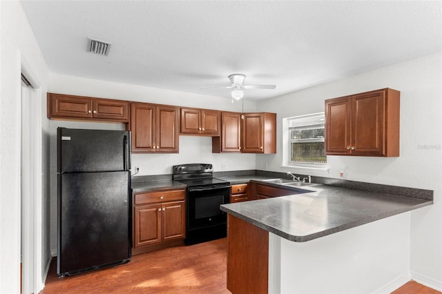 kitchen with dark wood-style floors, dark countertops, visible vents, a sink, and black appliances