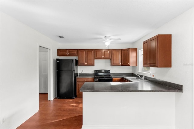 kitchen featuring dark countertops, dark wood-style flooring, a peninsula, black appliances, and a sink