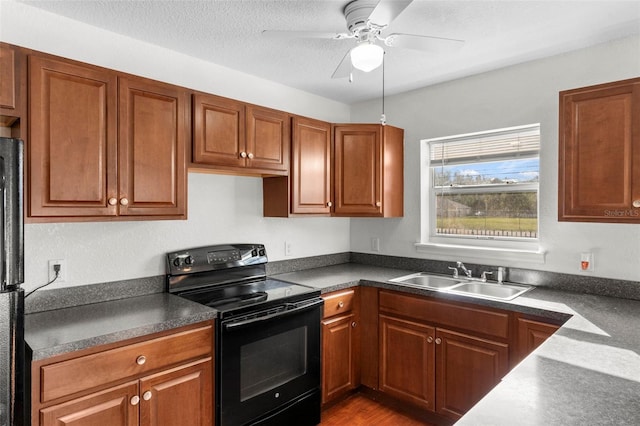 kitchen with brown cabinetry, dark countertops, a textured ceiling, black electric range, and a sink