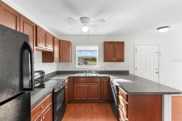 kitchen featuring a peninsula, a sink, dark wood-style floors, black appliances, and dark countertops