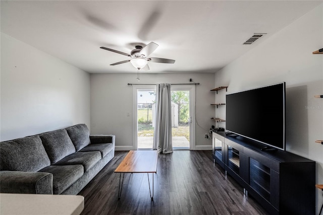 living room with dark wood-style floors, visible vents, baseboards, and a ceiling fan