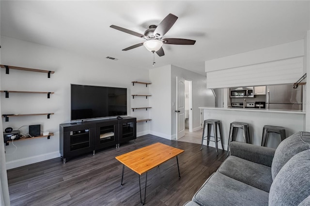 living room featuring dark wood-type flooring, visible vents, baseboards, and a ceiling fan