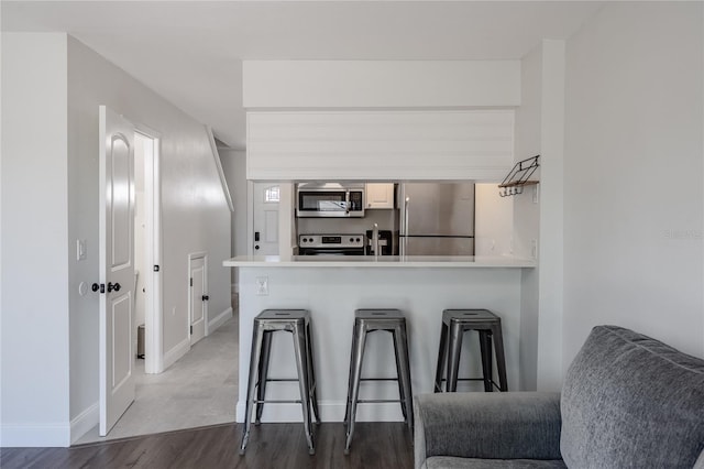 kitchen with appliances with stainless steel finishes, a breakfast bar, wood finished floors, a peninsula, and light countertops