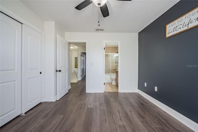 unfurnished bedroom featuring baseboards, visible vents, dark wood-type flooring, a textured ceiling, and a closet