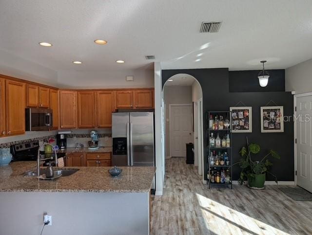 kitchen featuring arched walkways, a peninsula, visible vents, appliances with stainless steel finishes, and brown cabinetry