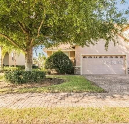 view of property hidden behind natural elements with a garage, decorative driveway, and stucco siding