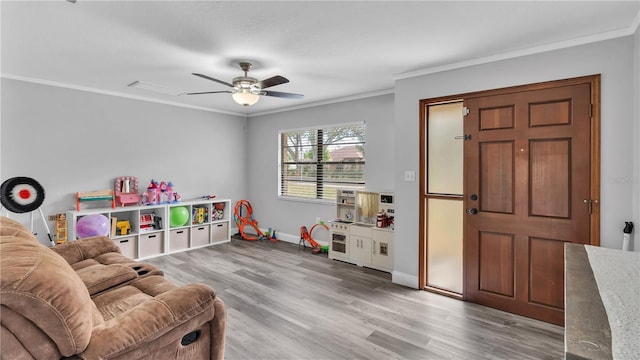 recreation room featuring light wood-style floors, crown molding, baseboards, and a ceiling fan