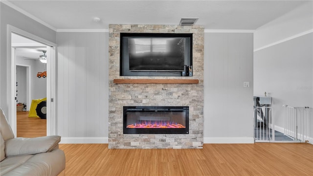 living room featuring a stone fireplace, wood finished floors, visible vents, and crown molding