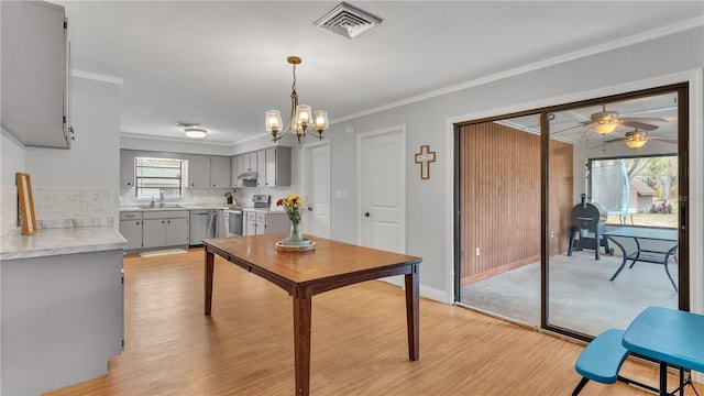 dining room featuring baseboards, visible vents, crown molding, light wood-type flooring, and ceiling fan with notable chandelier