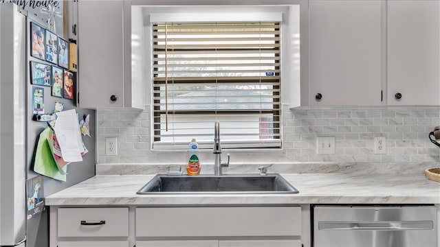 kitchen with light stone counters, stainless steel appliances, decorative backsplash, white cabinetry, and a sink