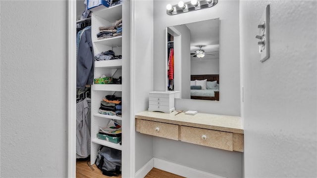 walk in closet with ceiling fan, built in desk, and light wood-type flooring