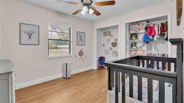 bedroom featuring a crib, light wood-style flooring, baseboards, and ceiling fan