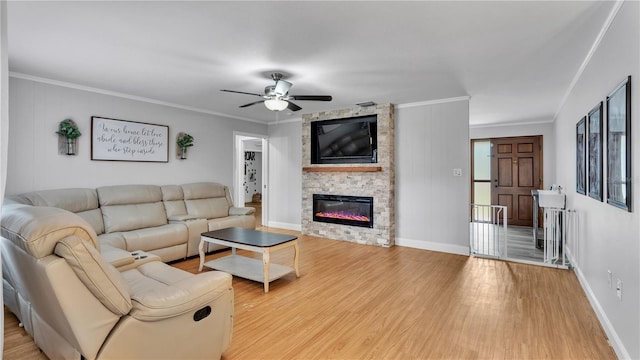 living area with light wood-style floors, baseboards, crown molding, and a stone fireplace