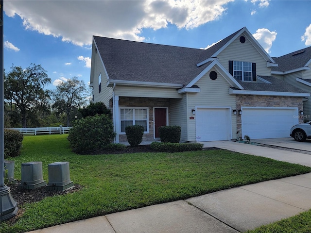 view of front of property featuring driveway, a garage, stone siding, fence, and a front yard