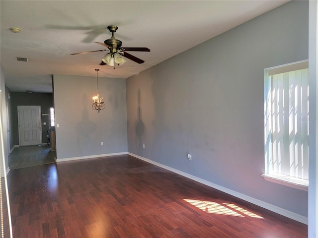 unfurnished room with dark wood-style floors, ceiling fan with notable chandelier, visible vents, and baseboards