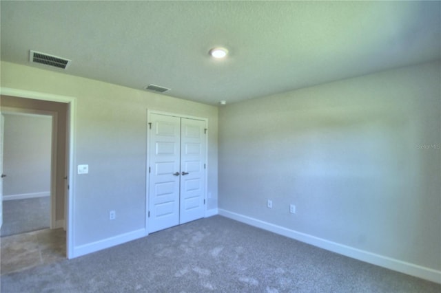 unfurnished bedroom with dark colored carpet, a closet, visible vents, and baseboards