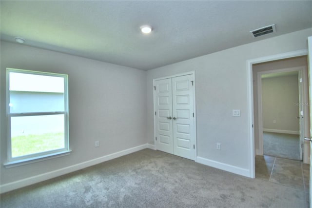 unfurnished bedroom featuring light carpet, baseboards, visible vents, and a closet