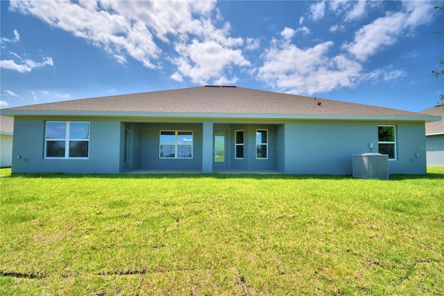 rear view of property with central AC, a yard, and stucco siding