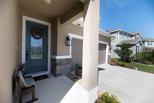 view of exterior entry with a residential view, stone siding, driveway, and stucco siding