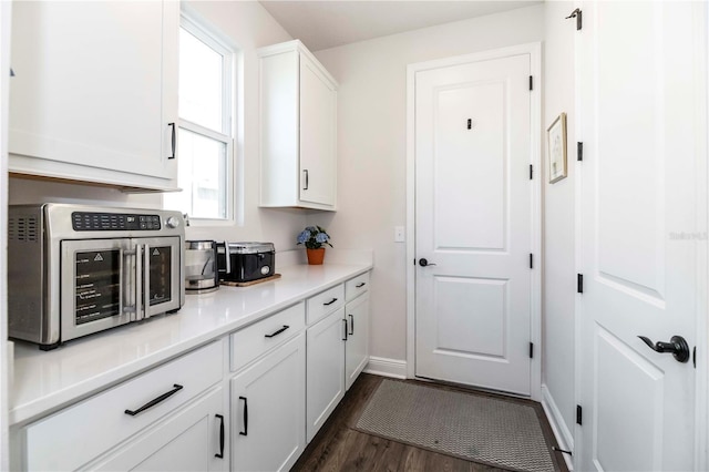 kitchen featuring white cabinetry, baseboards, light countertops, stainless steel microwave, and dark wood finished floors