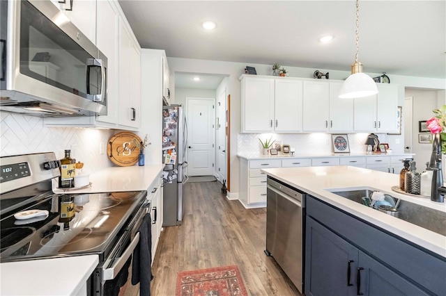 kitchen featuring white cabinets, light wood-style flooring, decorative light fixtures, stainless steel appliances, and light countertops