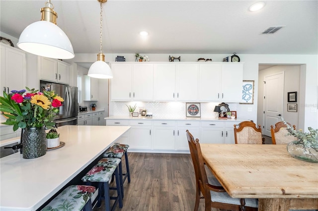 kitchen with visible vents, light countertops, a breakfast bar, and freestanding refrigerator