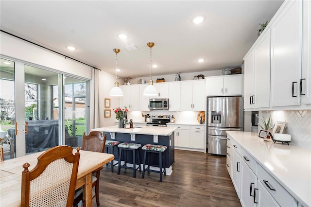 kitchen with dark wood-style floors, a breakfast bar area, light countertops, appliances with stainless steel finishes, and white cabinetry