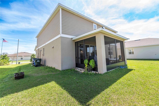 back of house featuring a sunroom, a lawn, and stucco siding