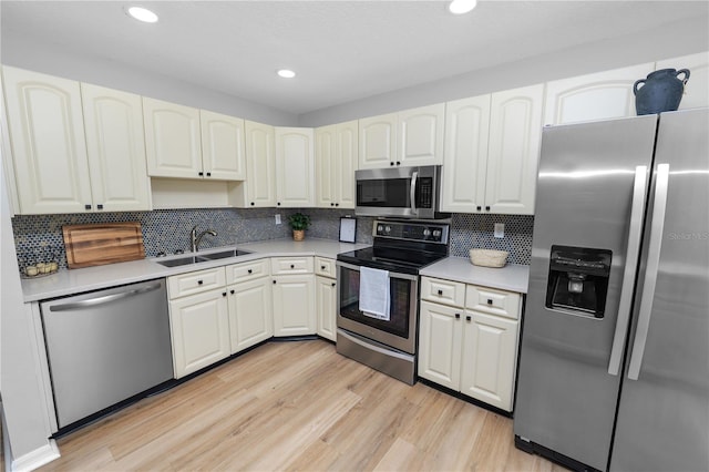 kitchen featuring stainless steel appliances, light wood-type flooring, a sink, and backsplash