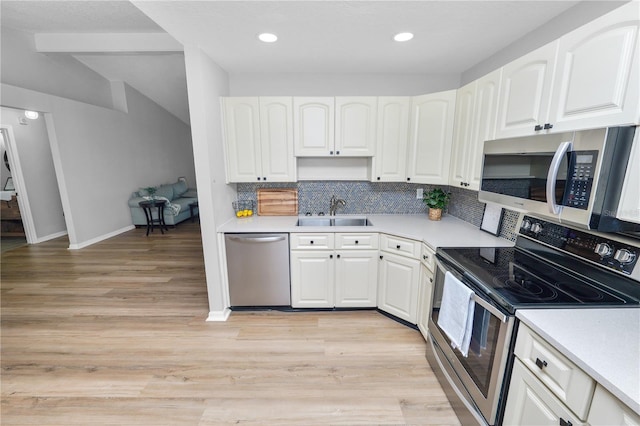 kitchen with light wood finished floors, decorative backsplash, appliances with stainless steel finishes, white cabinets, and a sink