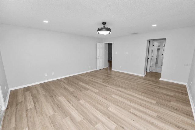 empty room with light wood finished floors, baseboards, a textured ceiling, and recessed lighting