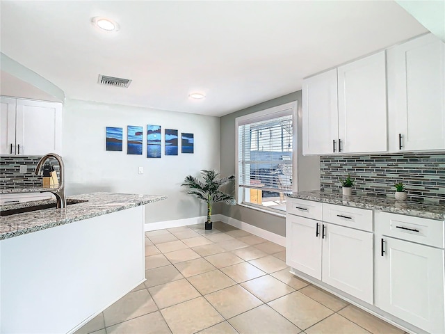 kitchen with light tile patterned floors, visible vents, white cabinets, light stone countertops, and tasteful backsplash