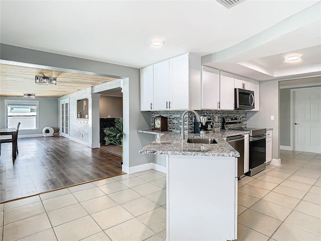 kitchen with light tile patterned floors, tasteful backsplash, appliances with stainless steel finishes, a sink, and light stone countertops