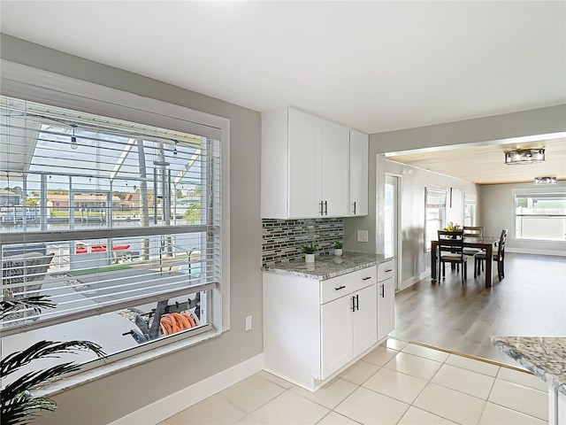 kitchen with light tile patterned floors, baseboards, white cabinets, light stone counters, and backsplash