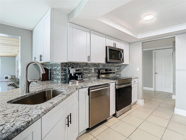 kitchen featuring a sink, white cabinetry, appliances with stainless steel finishes, a tray ceiling, and tasteful backsplash