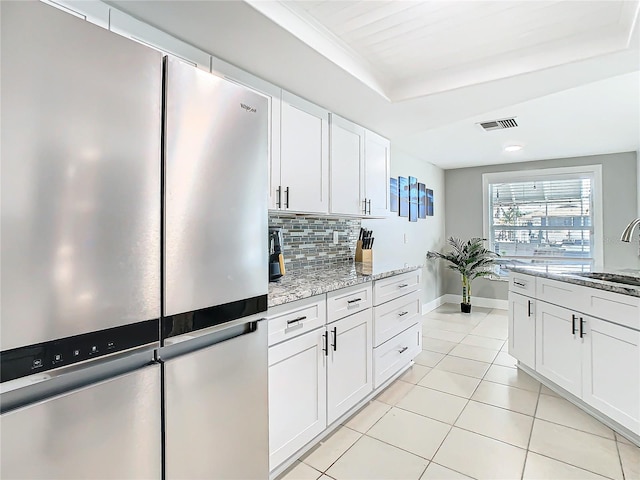 kitchen with light tile patterned floors, visible vents, decorative backsplash, freestanding refrigerator, and white cabinetry