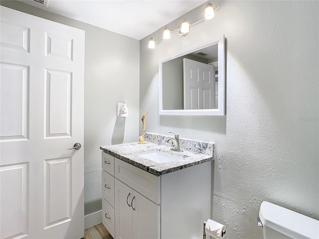 half bathroom featuring a textured wall, vanity, and toilet