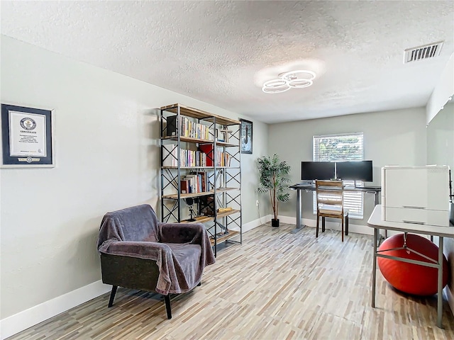 office featuring a textured ceiling, wood finished floors, visible vents, and baseboards