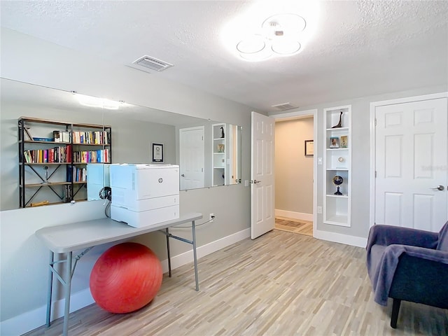 office space featuring light wood-type flooring, visible vents, a textured ceiling, and baseboards