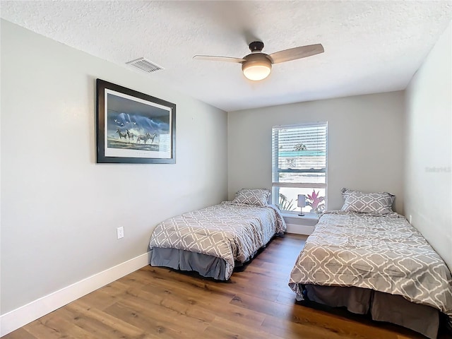 bedroom with baseboards, visible vents, ceiling fan, wood finished floors, and a textured ceiling