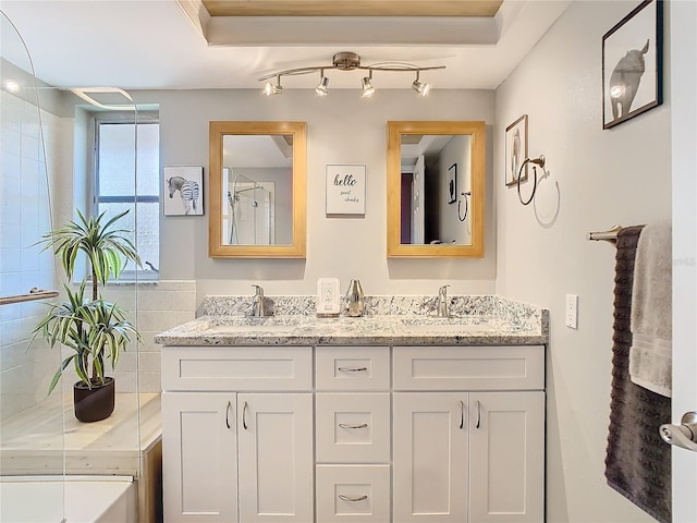 bathroom featuring double vanity, tiled shower, and a sink