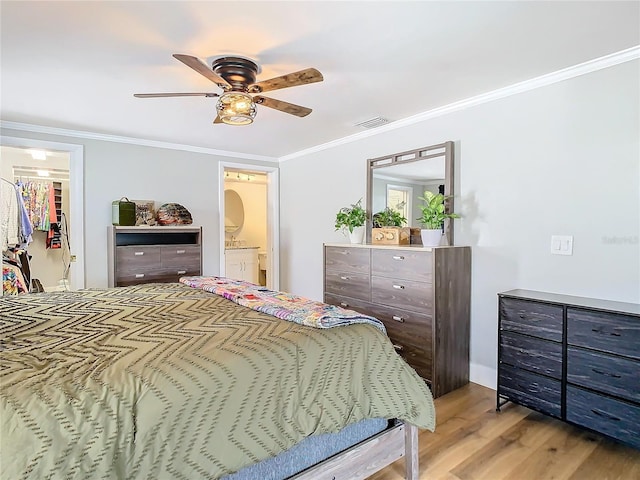 bedroom with visible vents, a ceiling fan, ornamental molding, light wood-type flooring, and a walk in closet