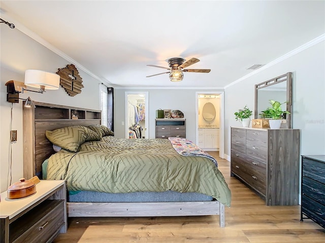 bedroom featuring light wood finished floors, visible vents, a walk in closet, and crown molding