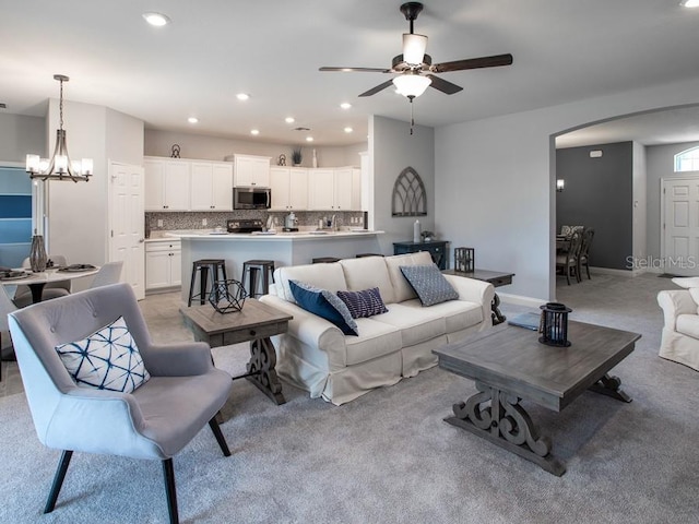 living area with arched walkways, recessed lighting, ceiling fan with notable chandelier, light colored carpet, and baseboards