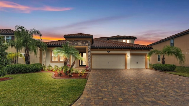 mediterranean / spanish-style home featuring an attached garage, a tiled roof, decorative driveway, stucco siding, and a front lawn