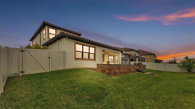 rear view of house featuring a yard, a fenced backyard, a gate, and stucco siding