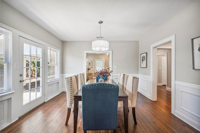 dining area with dark wood-type flooring, a decorative wall, wainscoting, and a notable chandelier