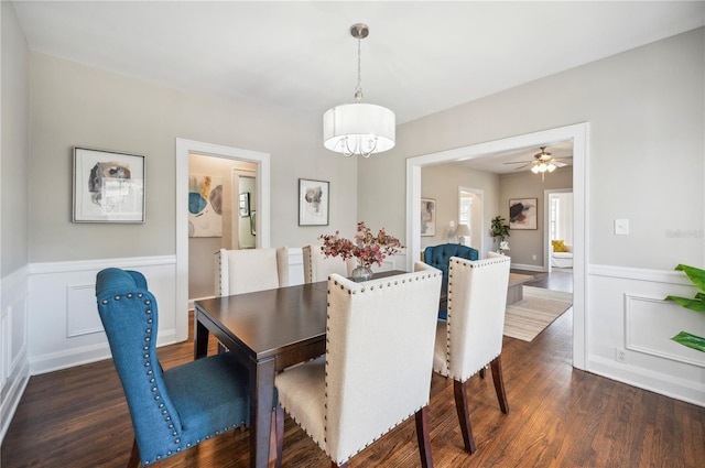 dining space with dark wood-style flooring, wainscoting, and a decorative wall