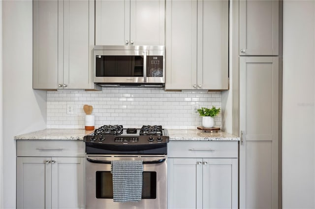 kitchen featuring stainless steel appliances, backsplash, gray cabinets, and light stone countertops